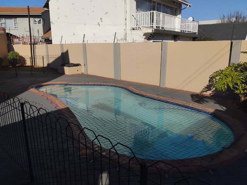 A private swimming pool area featuring a paved surround, enclosed by a perimeter wall with electric fencing and a metal safety fence.