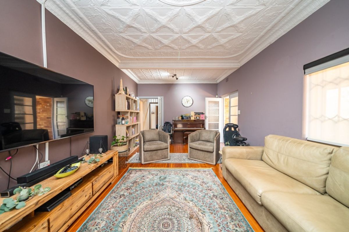 A living room featuring a decorative pressed metal ceiling and original hardwood flooring, offering a character-filled space with potential for modern updates.