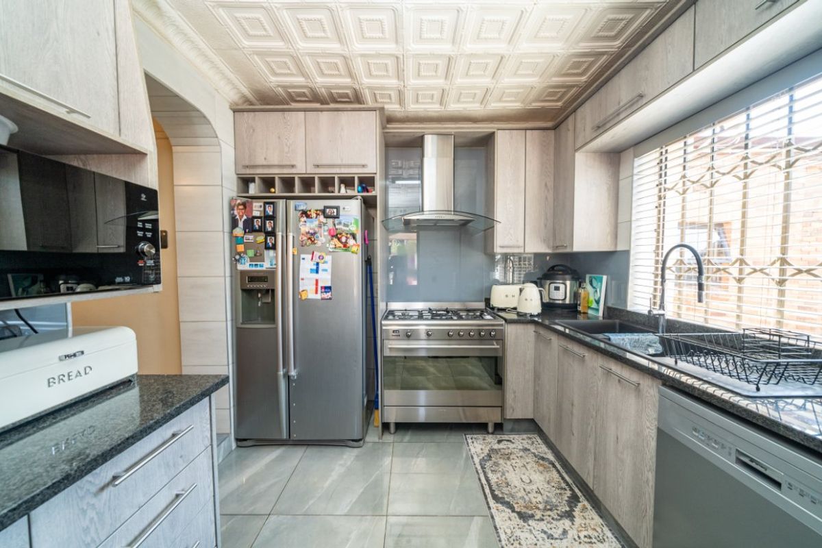 A well-appointed kitchen featuring light wood-grain cabinetry, granite countertops, a gas stove with extractor fan, and a distinctive coffered ceiling.