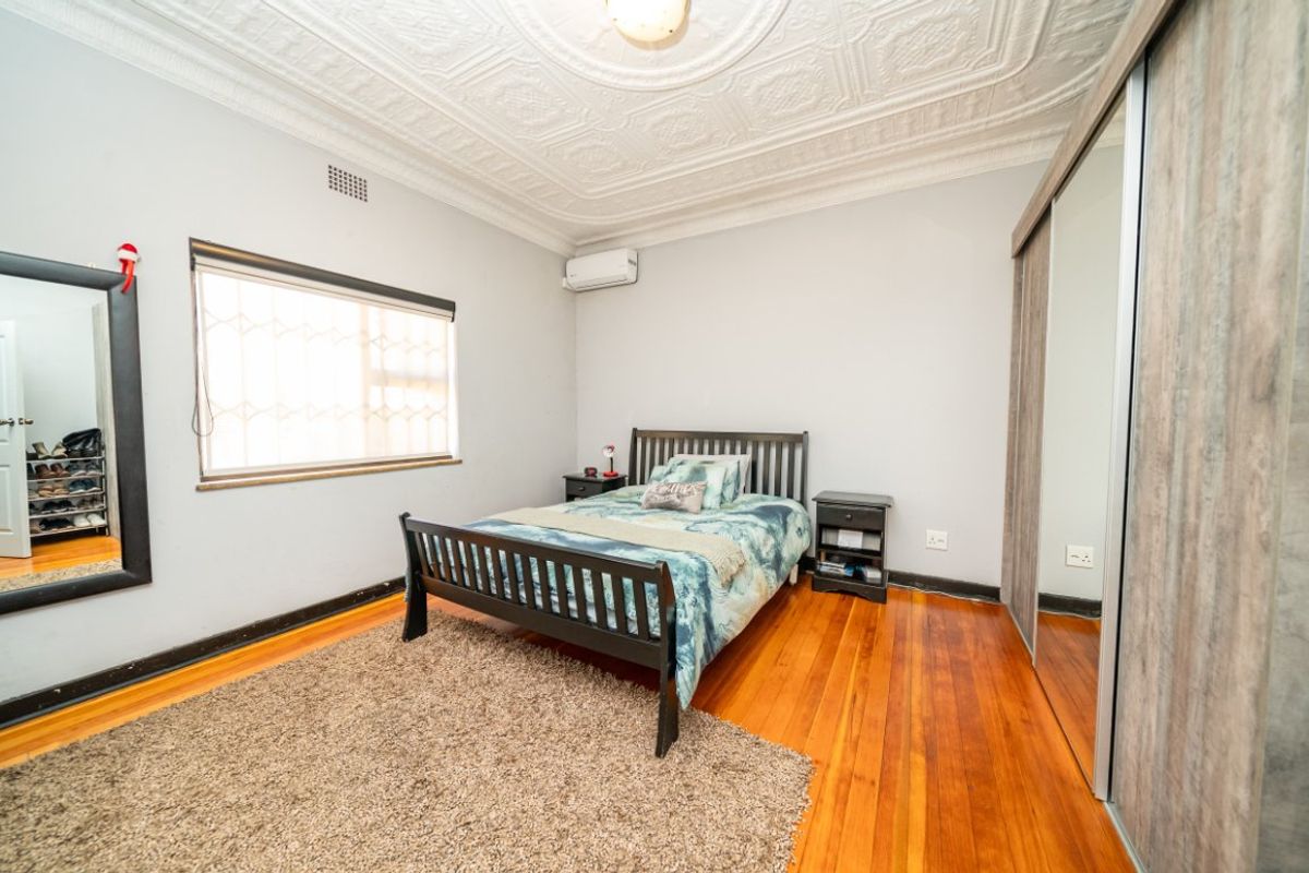 Spacious bedroom featuring original pressed metal ceilings, polished hardwood flooring, and a large built-in sliding wardrobe with mirrored panels.
