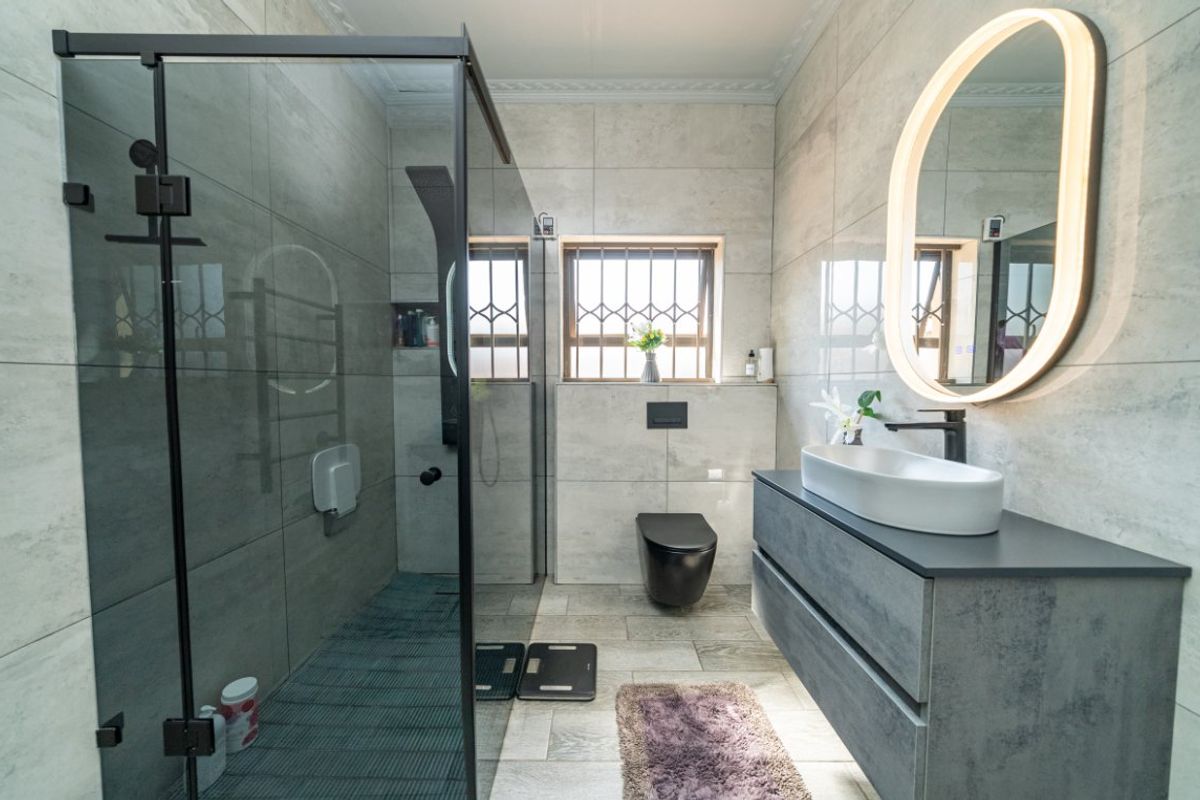 Modern, well-appointed bathroom featuring a spacious walk-in shower, wall-hung toilet, sleek vanity with vessel sink, and contemporary backlit mirror.