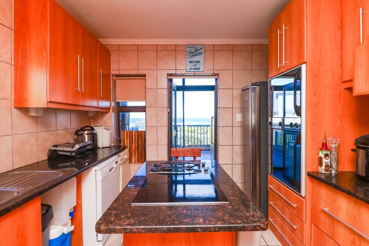 A functional kitchen featuring warm-toned cabinetry, granite countertops, a central island with a built-in hob, and integrated double ovens.