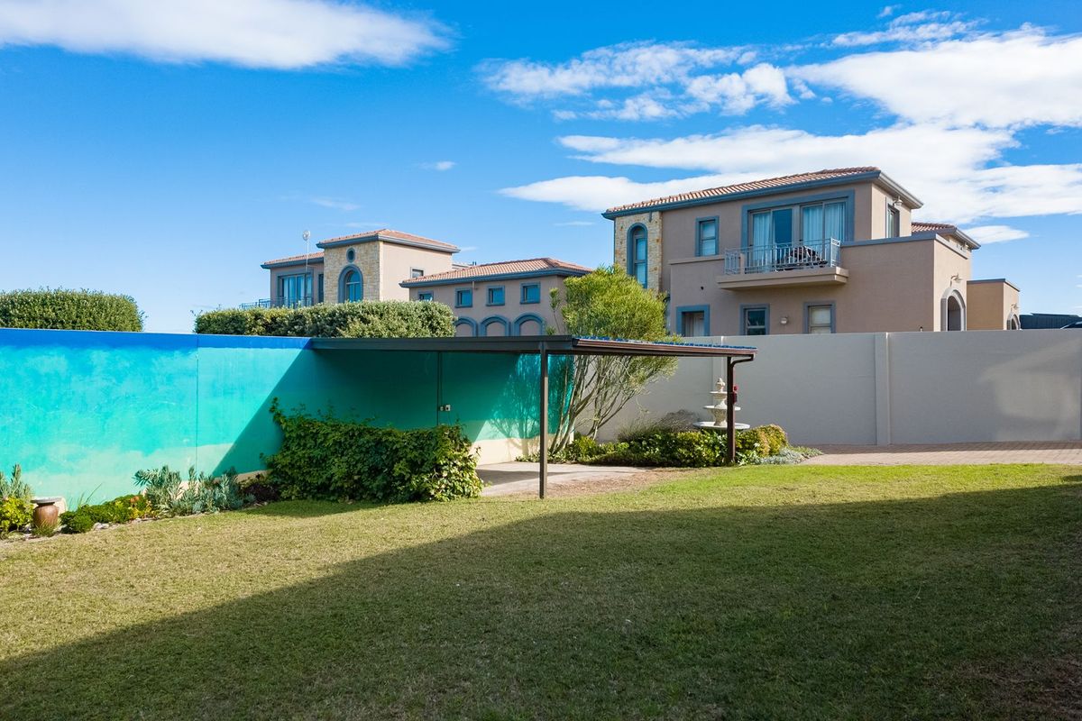 A well-maintained rear garden featuring a covered patio area, paved sections, and a painted boundary wall, set against a clear blue sky.