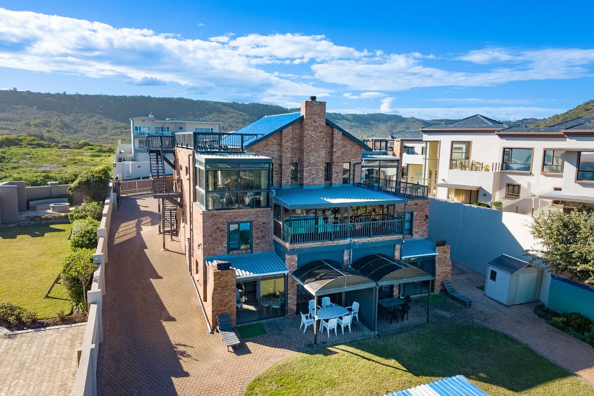 Aerial view of a multi-story brick house featuring a metal roof, multiple balconies, and a paved driveway in a coastal setting.