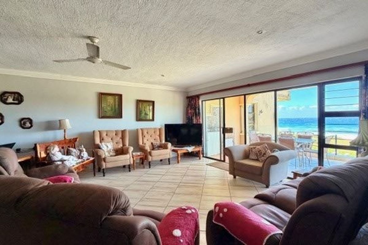 Spacious living room featuring tiled flooring, a ceiling fan, and large sliding glass doors that provide direct access to a balcony with ocean views.