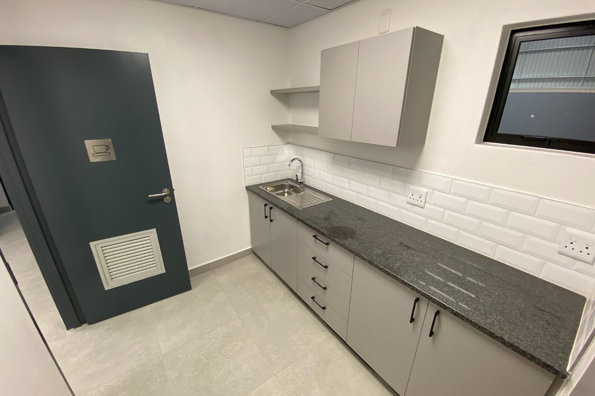 A clean, modern kitchenette featuring grey cabinetry, stone countertops, a stainless steel sink, and a classic subway tile backsplash.