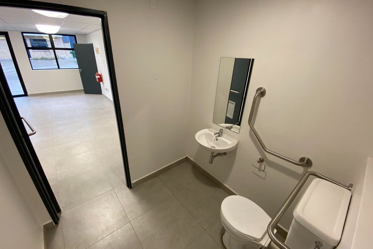 A clean, accessible bathroom featuring a wall-mounted basin, toilet, and safety grab rails, with tiled flooring and neutral finishes.