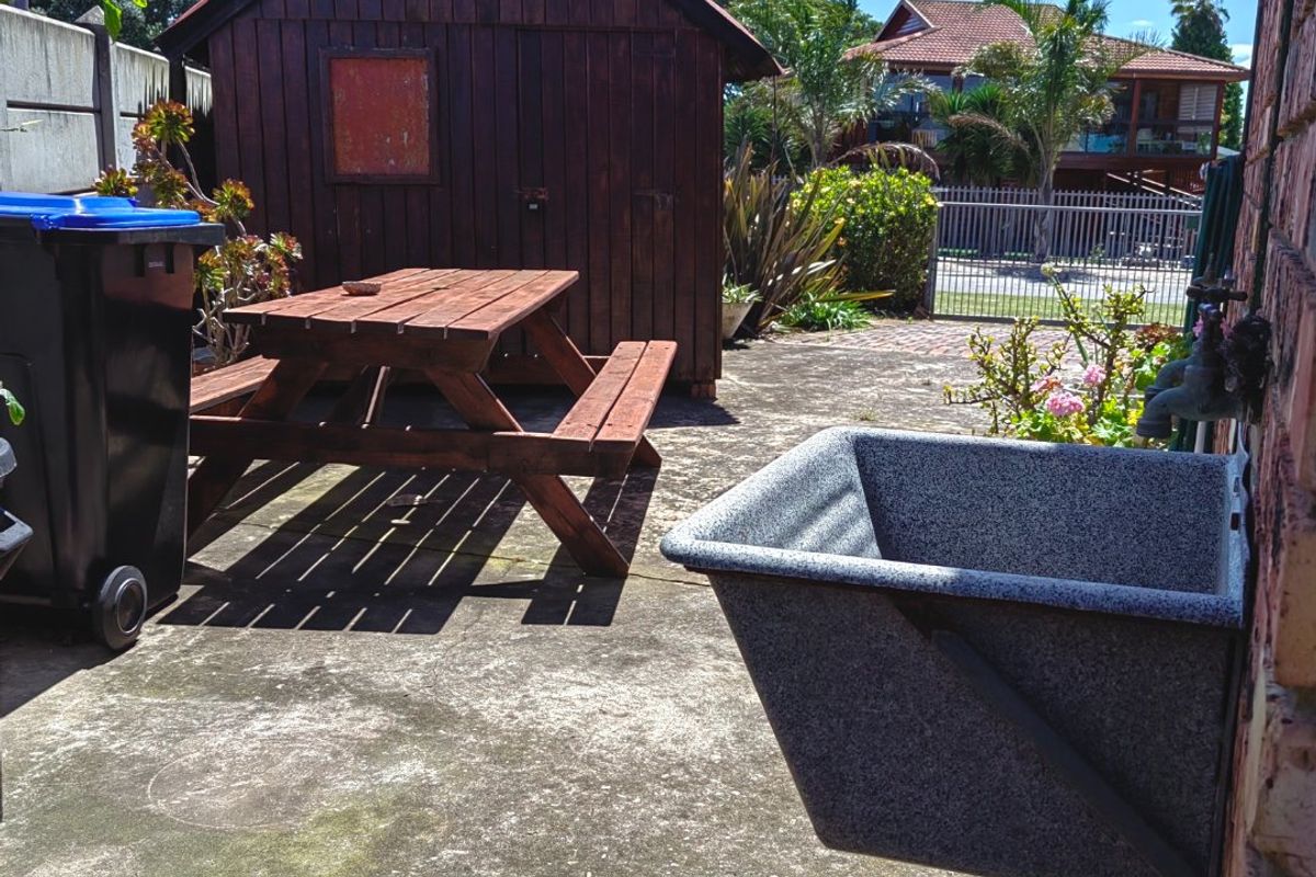 Rear exterior area featuring a concrete patio, utility sink, and a wooden storage shed.