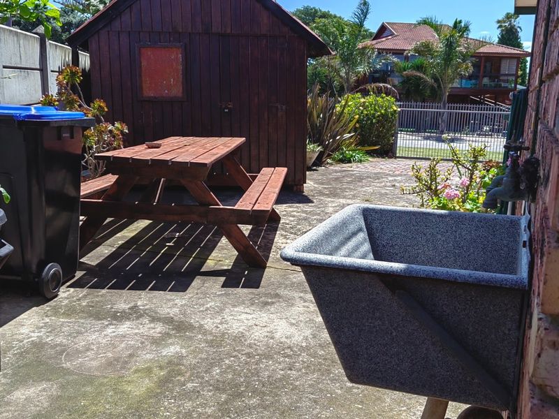Rear exterior area featuring a concrete patio, utility sink, and a wooden storage shed.