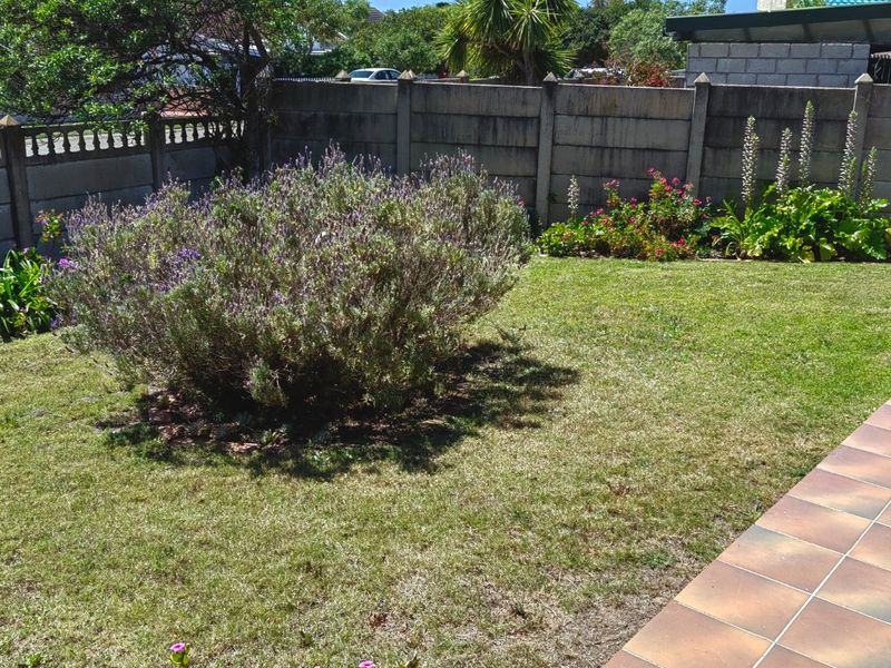 A private rear garden featuring a well-maintained lawn, established shrubbery, and a tiled patio area enclosed by a precast concrete boundary wall.