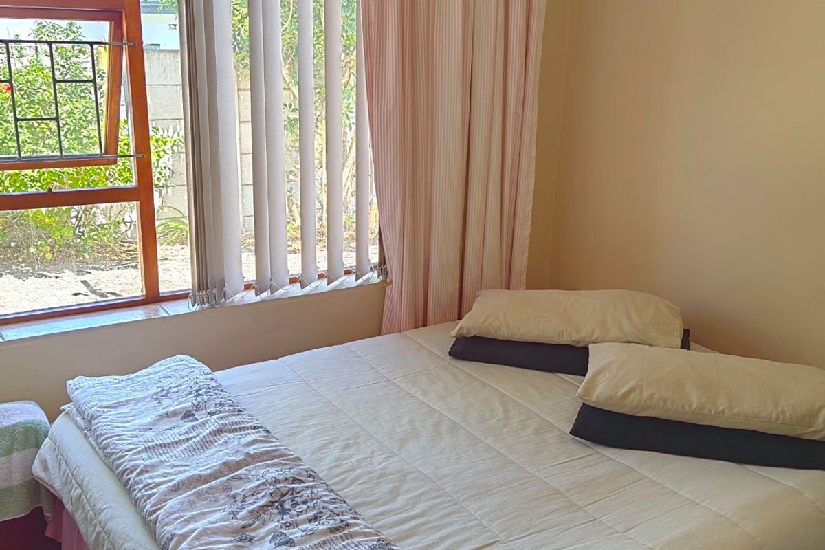 A bedroom featuring tiled flooring and a large wooden-framed window with vertical blinds, providing natural light and a view of the exterior.
