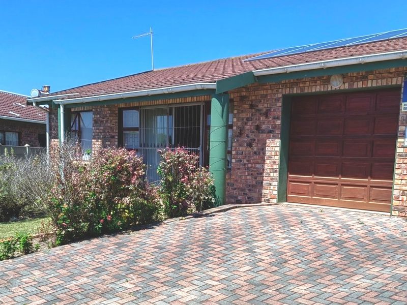 Front exterior view of a brick house featuring a paved driveway, single garage, and solar panels installed on the tiled roof.