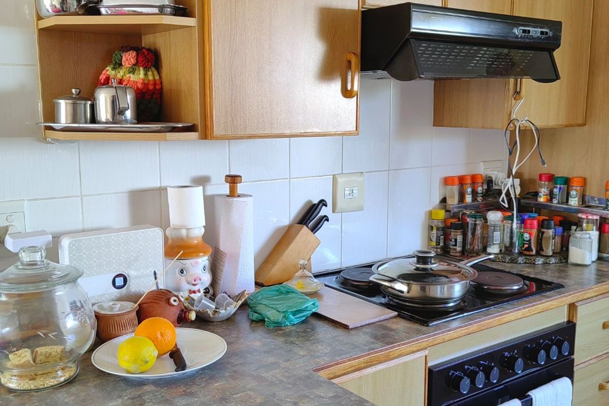 A functional kitchen featuring wood-look laminate cabinetry, a tiled backsplash, and integrated cooking appliances including an oven, hob, and extractor fan.