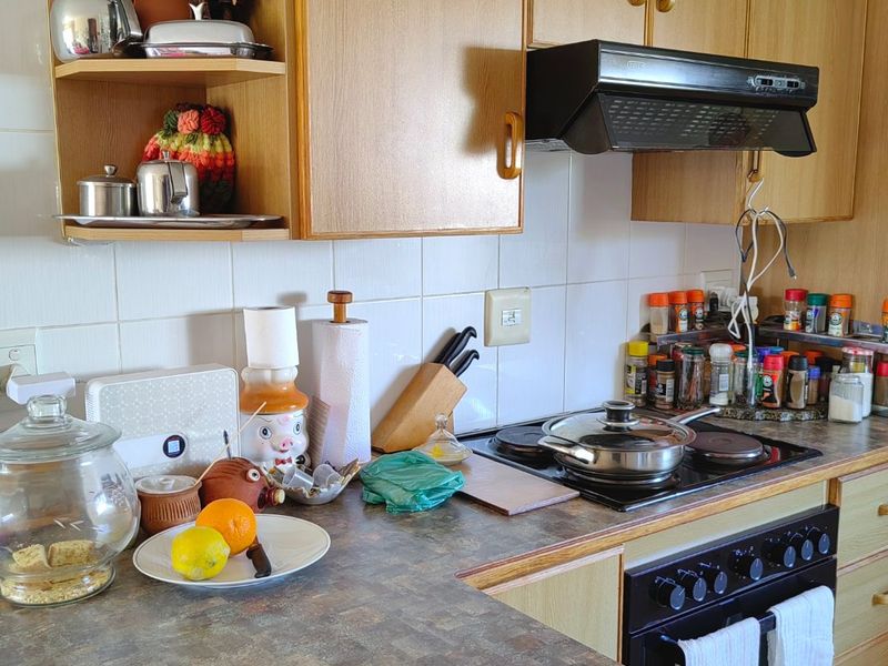 A functional kitchen featuring wood-look laminate cabinetry, a tiled backsplash, and integrated cooking appliances including an oven, hob, and extractor fan.