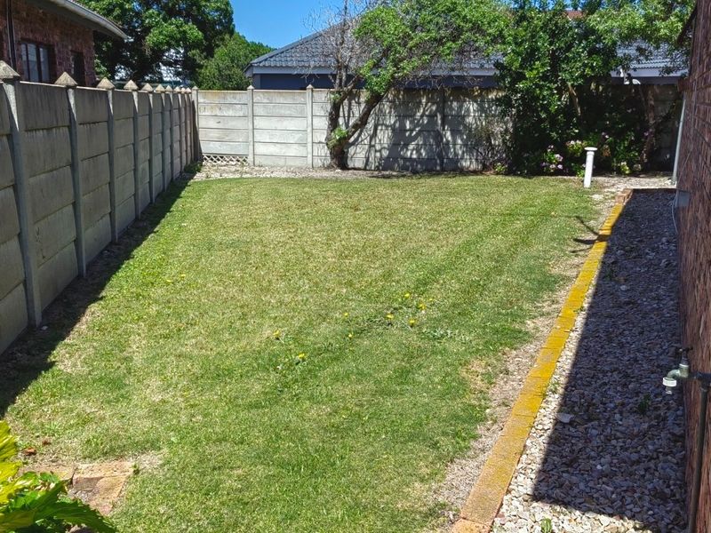 A private rear garden featuring a well-maintained lawn, gravel border with brick edging, and secure precast concrete boundary walls.