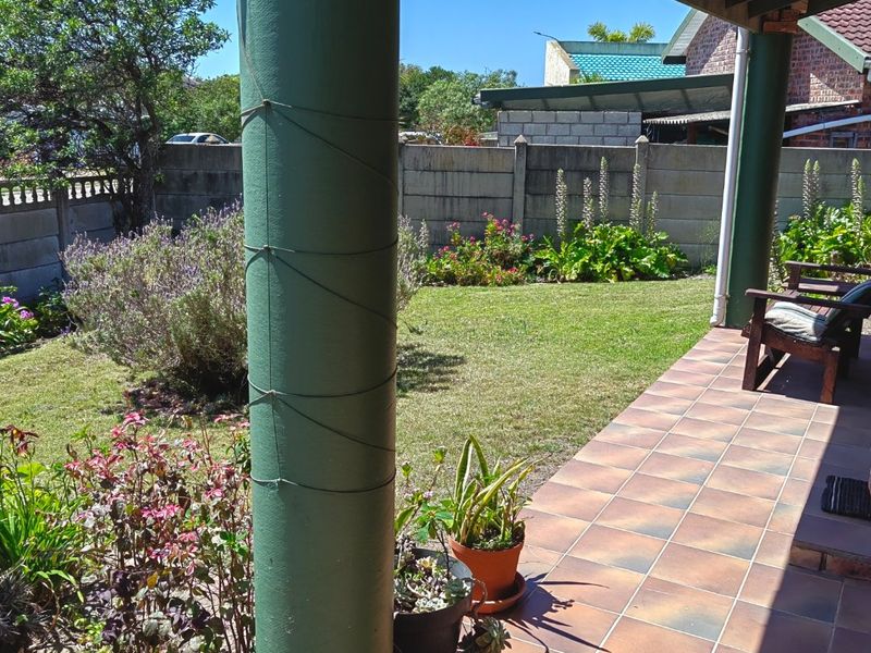A covered patio area featuring tiled flooring and structural columns, overlooking a private garden with a precast concrete boundary wall.