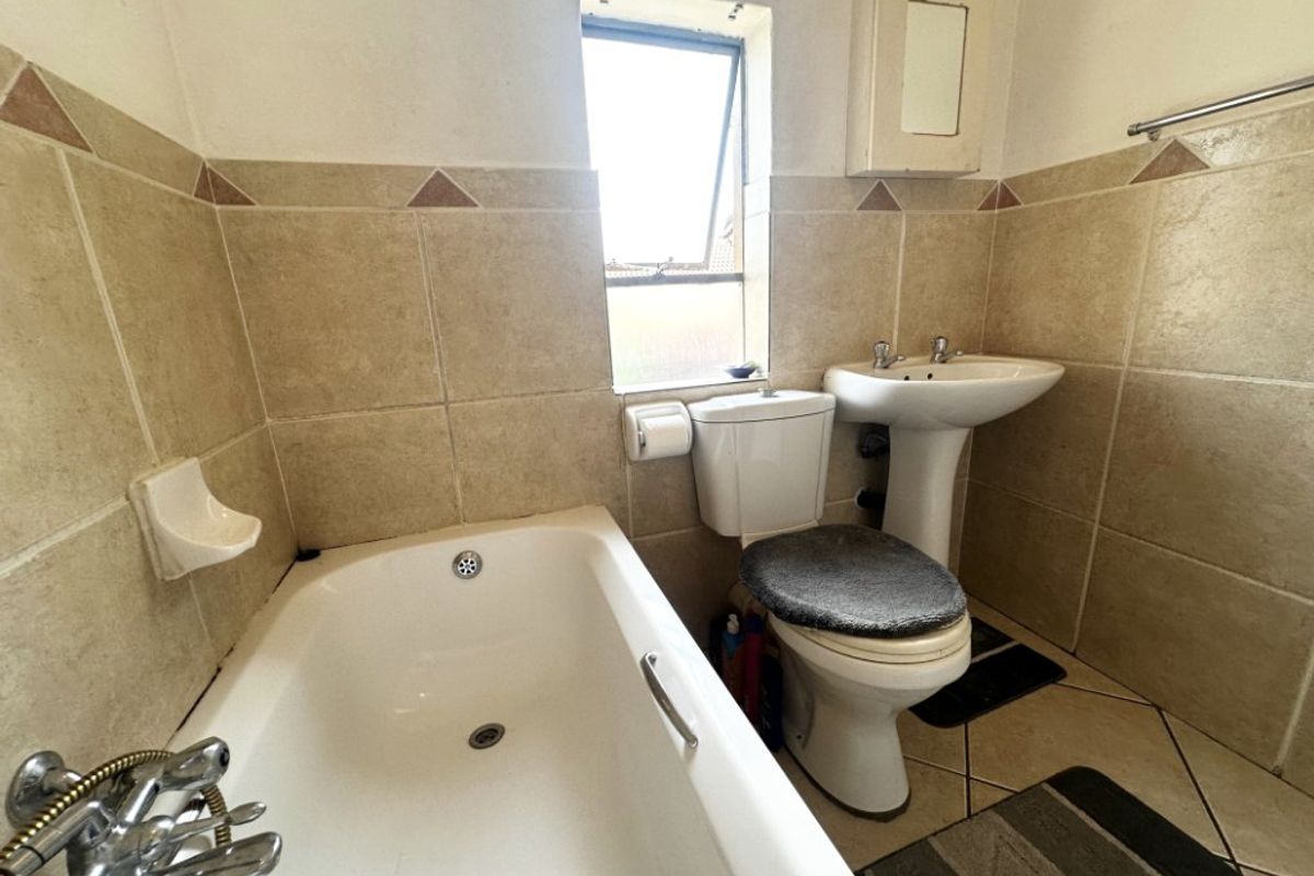 A functional bathroom featuring a bathtub, pedestal basin, and toilet with neutral wall and floor tiling.