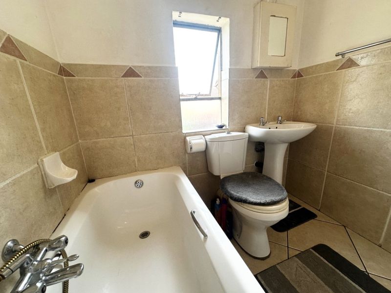 A functional bathroom featuring a bathtub, pedestal basin, and toilet with neutral wall and floor tiling.