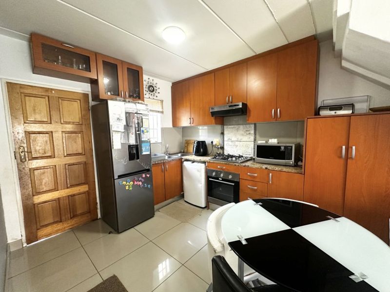 A functional kitchen featuring wood-finish cabinetry, tiled flooring, and integrated appliances, offering a practical layout for daily cooking and meal preparation.