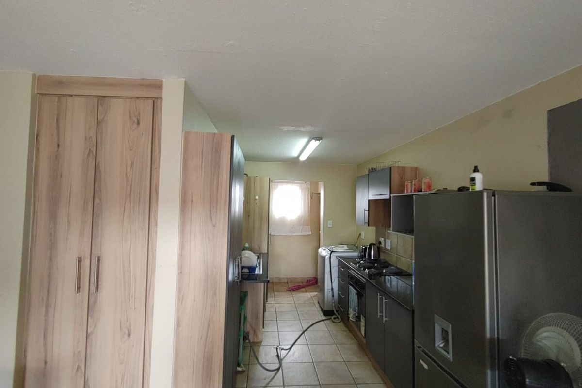 A functional kitchen area featuring dark cabinetry, a gas hob, and tiled flooring, showing signs of ceiling wear and requiring cosmetic updates.