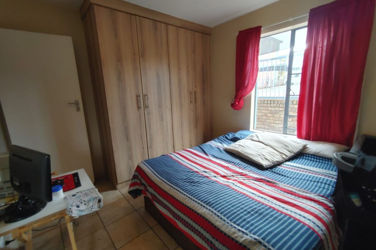 A functional bedroom featuring built-in wooden wardrobes, tiled flooring, and a window with security bars, providing a practical living space.