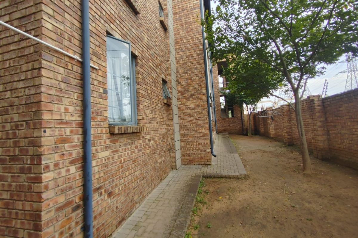 A view of the rear exterior of the apartment building featuring face brick walls, a paved walkway, and a perimeter boundary wall.