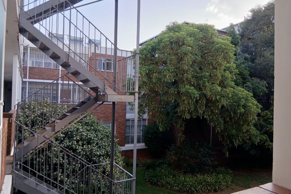View of the apartment complex rear exterior featuring a metal staircase, brick building facade, and established garden area.