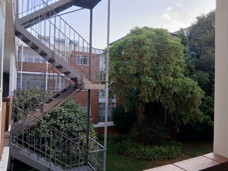 View of the apartment complex rear exterior featuring a metal staircase, brick building facade, and established garden area.