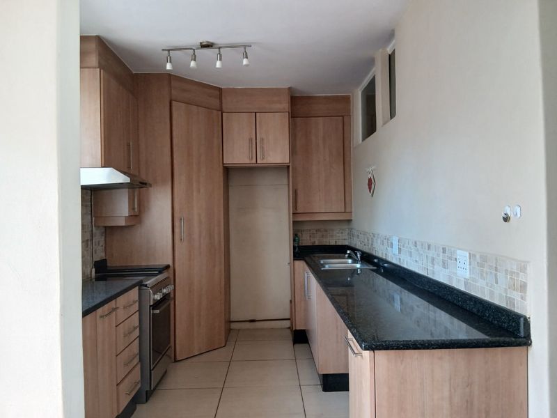 A clean, functional kitchen featuring light wood-finish cabinetry, dark granite countertops, a mosaic tile backsplash, and integrated stainless steel appliances.