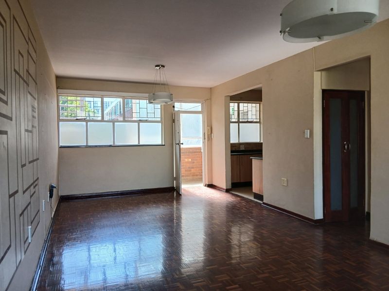 Spacious open-plan living area featuring polished parquet flooring, neutral walls, and direct access to a balcony, with an adjoining kitchen space.