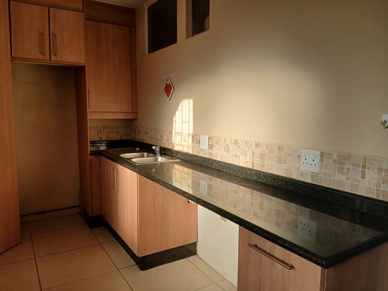 A functional kitchen featuring laminate cabinetry, granite countertops, a double basin sink, and a tiled backsplash with neutral ceramic flooring.
