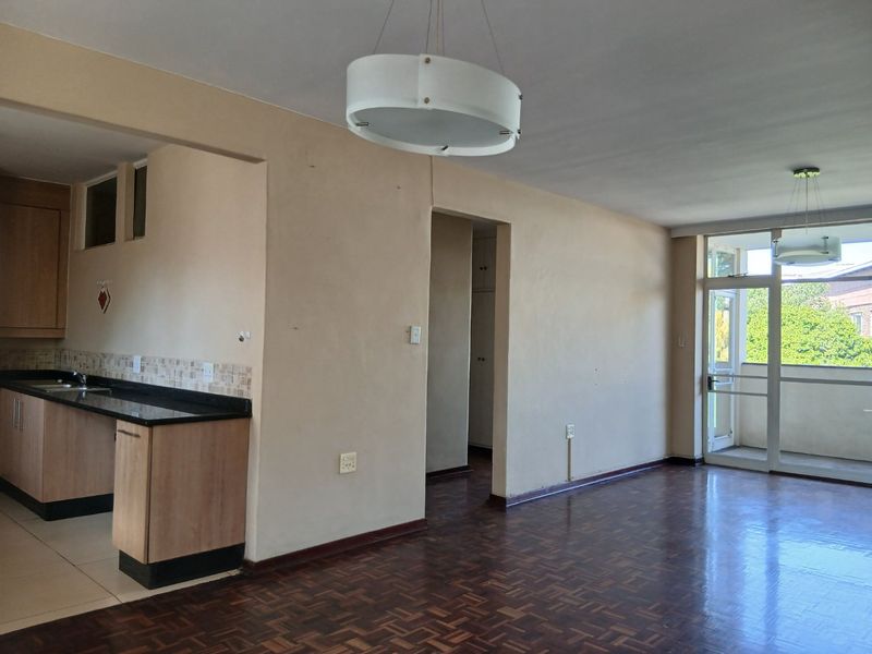 Open plan living area featuring parquet flooring, a compact kitchen with granite countertops, and direct access to a balcony through a glass door.