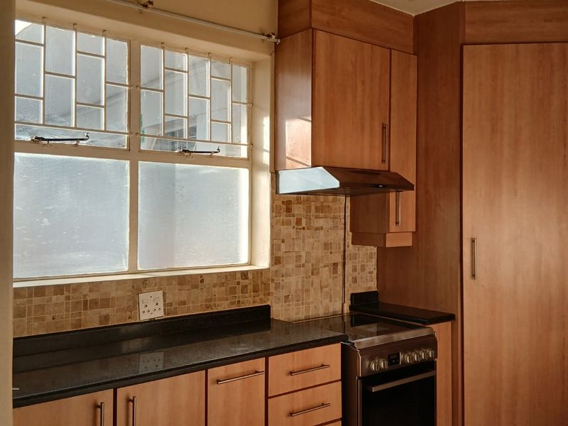 A functional kitchen featuring wood-finish cabinetry, dark granite countertops, a mosaic tile backsplash, and a built-in stove with an extractor fan.