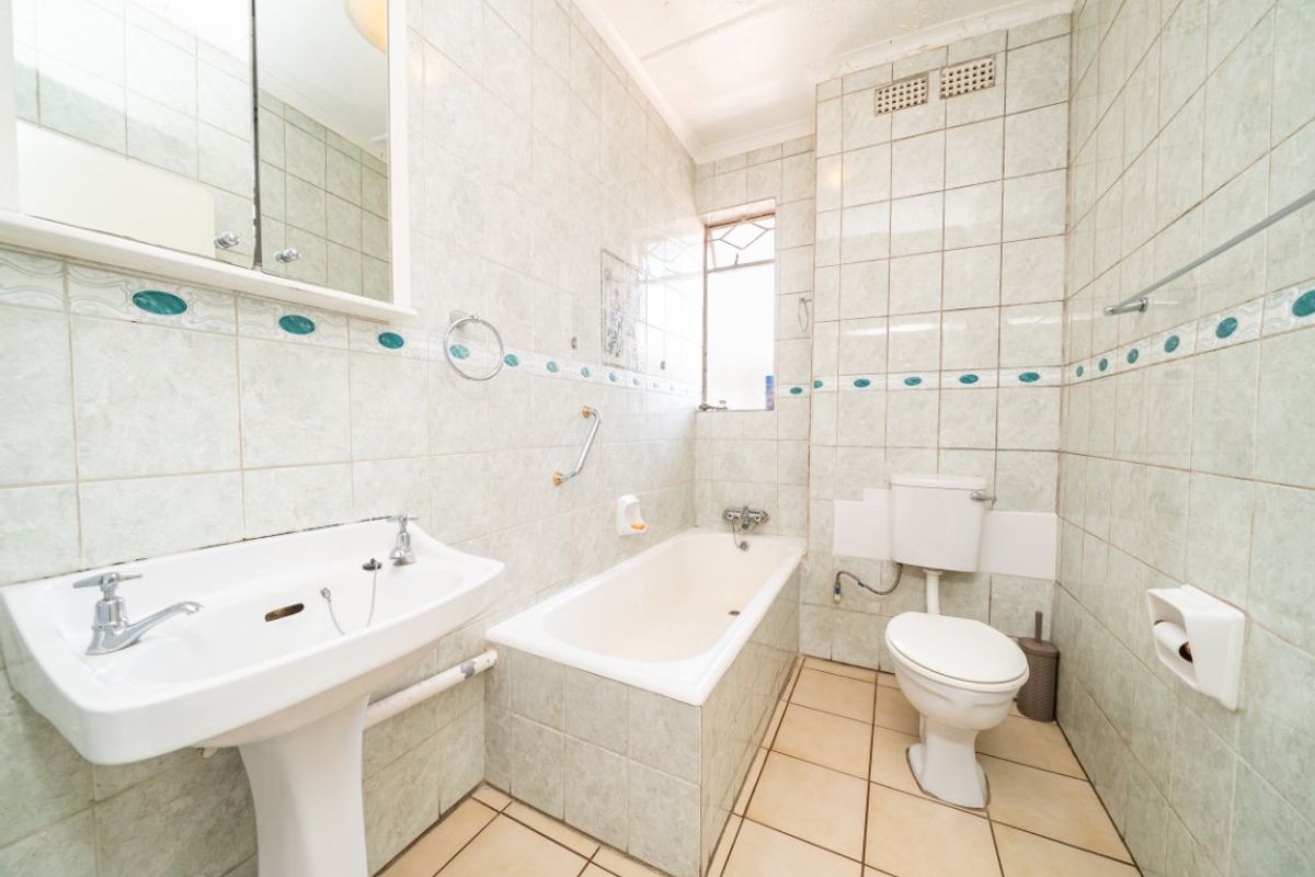 A dated bathroom featuring a pedestal basin, built-in bathtub, and toilet, finished with full-height wall tiling and floor tiles.