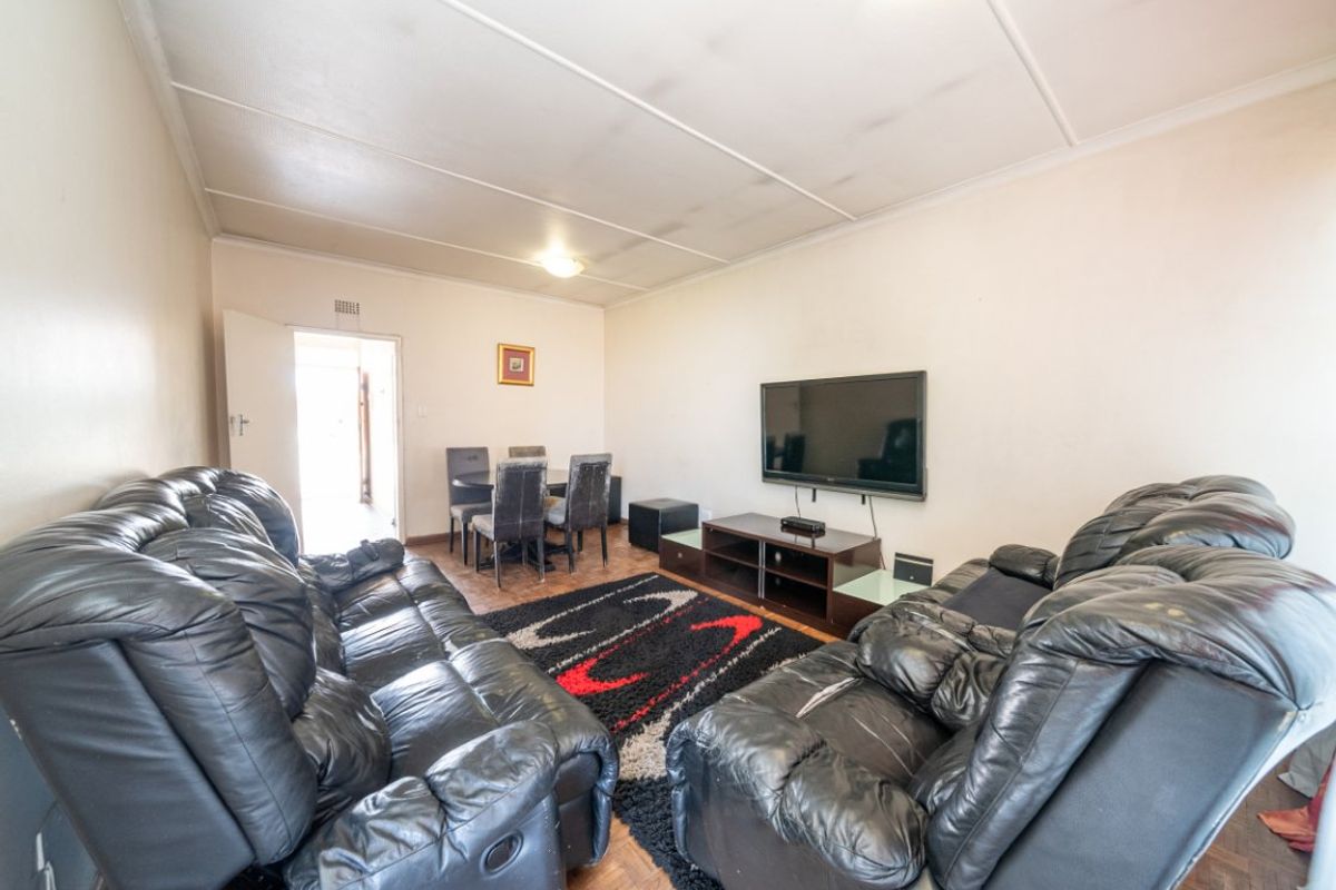 A living room featuring parquet flooring and ceiling tiles, offering a functional space with potential for cosmetic updates.