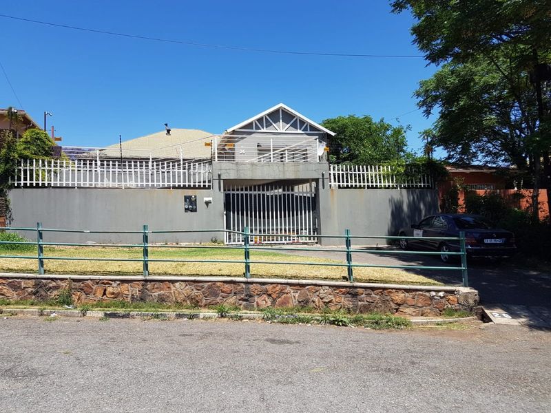 Front elevation of the property featuring a secure perimeter wall, metal sliding gate, and stone retaining wall along the street frontage.
