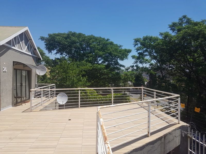 Spacious elevated balcony featuring tiled flooring and a metal balustrade, offering an open outdoor area with views of the surrounding trees.