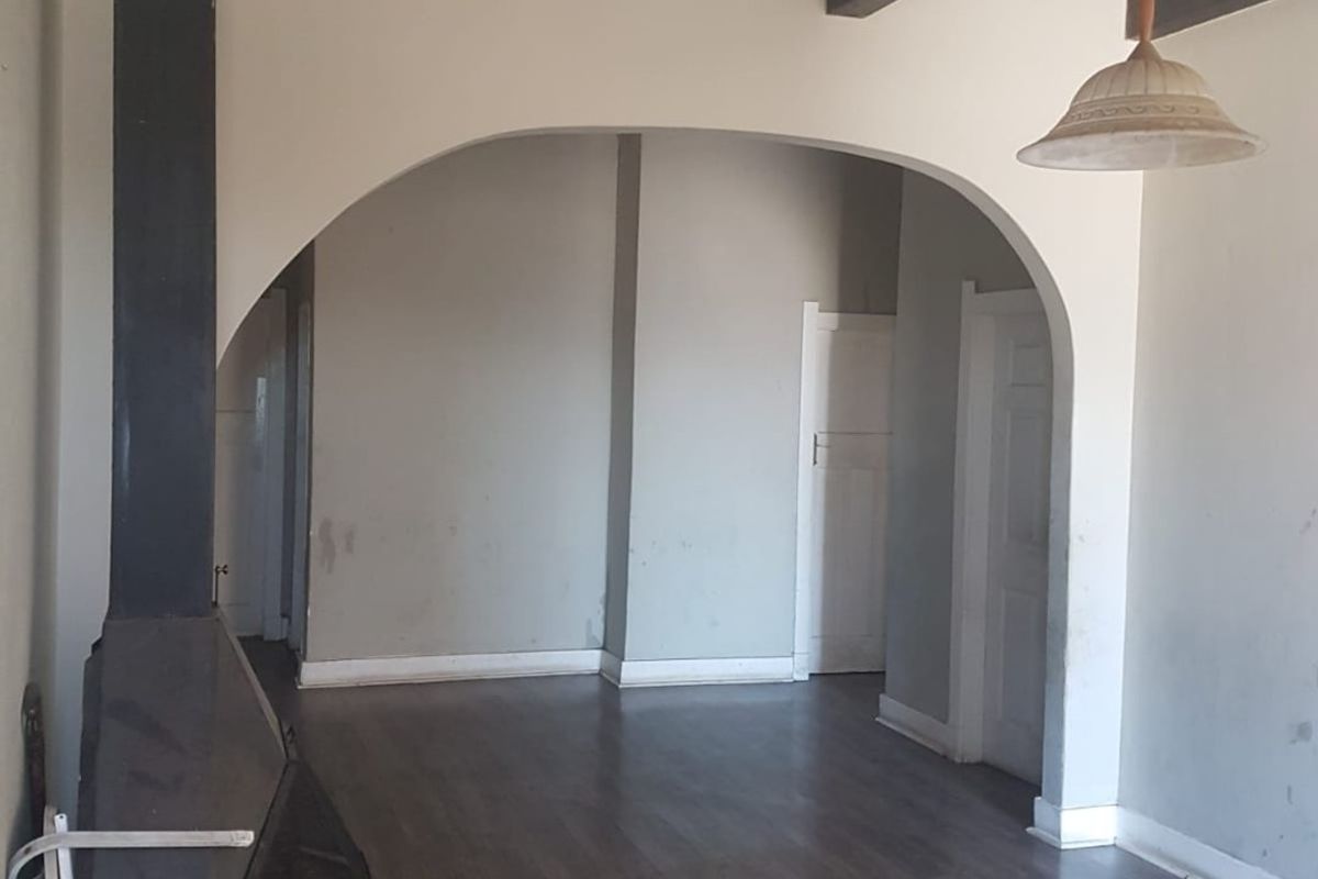 An empty living room featuring exposed ceiling beams, a freestanding fireplace, and an arched doorway leading to an adjacent space.