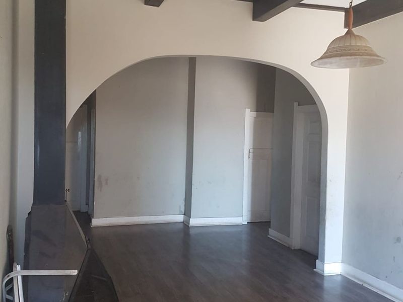 An empty living room featuring exposed ceiling beams, a freestanding fireplace, and an arched doorway leading to an adjacent space.