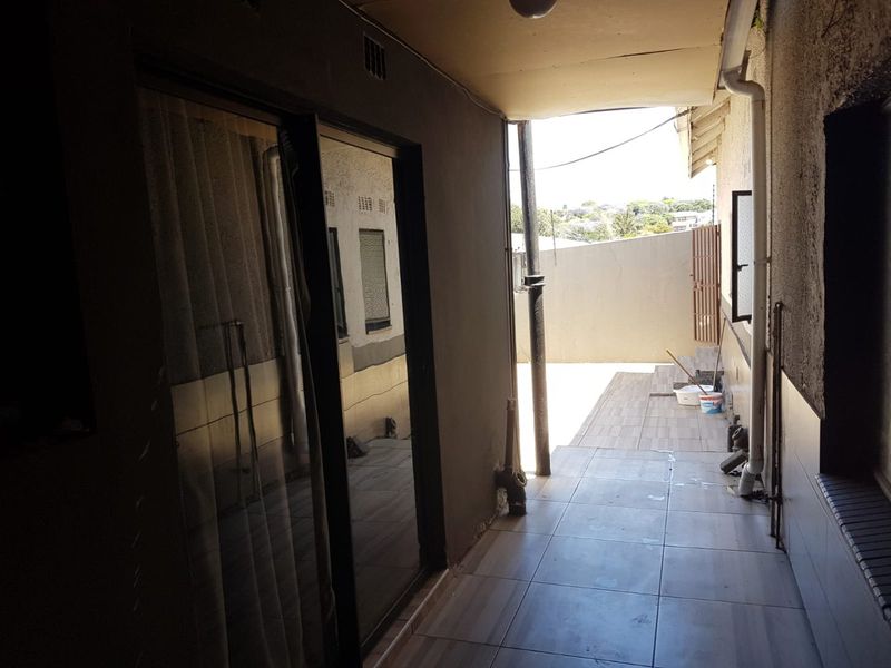 A covered outdoor patio area featuring tiled flooring and sliding glass door access, requiring some maintenance to the ceiling and wall finishes.