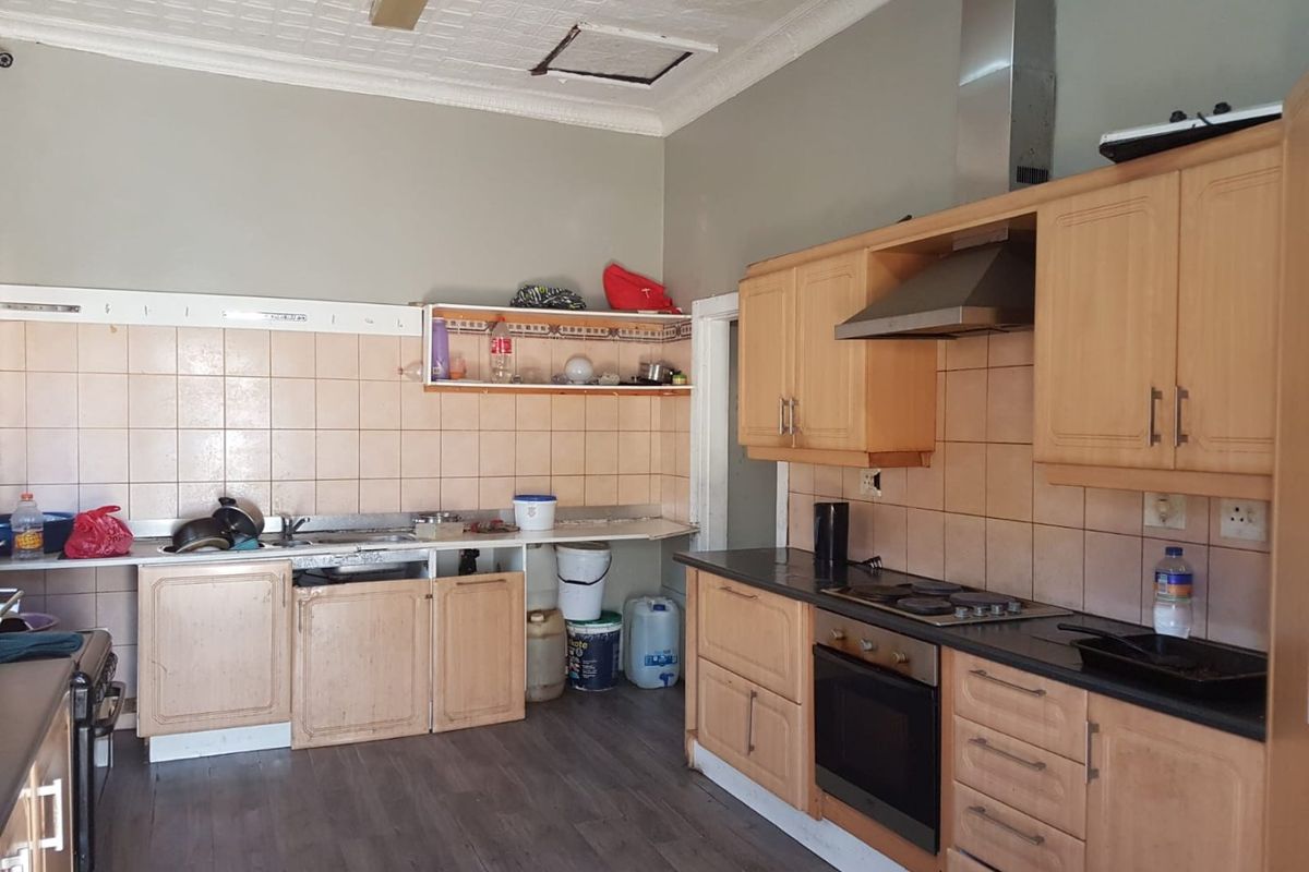 A functional kitchen featuring built-in wooden cabinetry, a stainless steel extractor fan, and an integrated oven, requiring cosmetic updates to improve its overall condition.