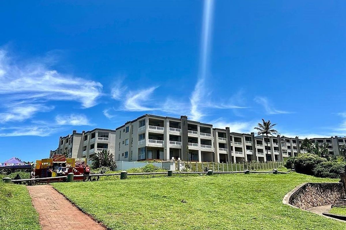 Exterior view of the apartment complex featuring multi-story residential blocks with balconies, set against a landscaped lawn and clear blue sky.