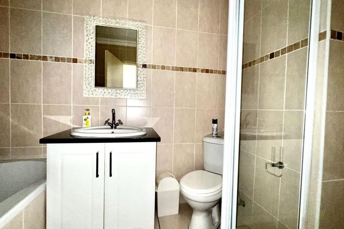 A functional bathroom featuring a vanity basin, toilet, shower enclosure, and bathtub with neutral wall tiling.