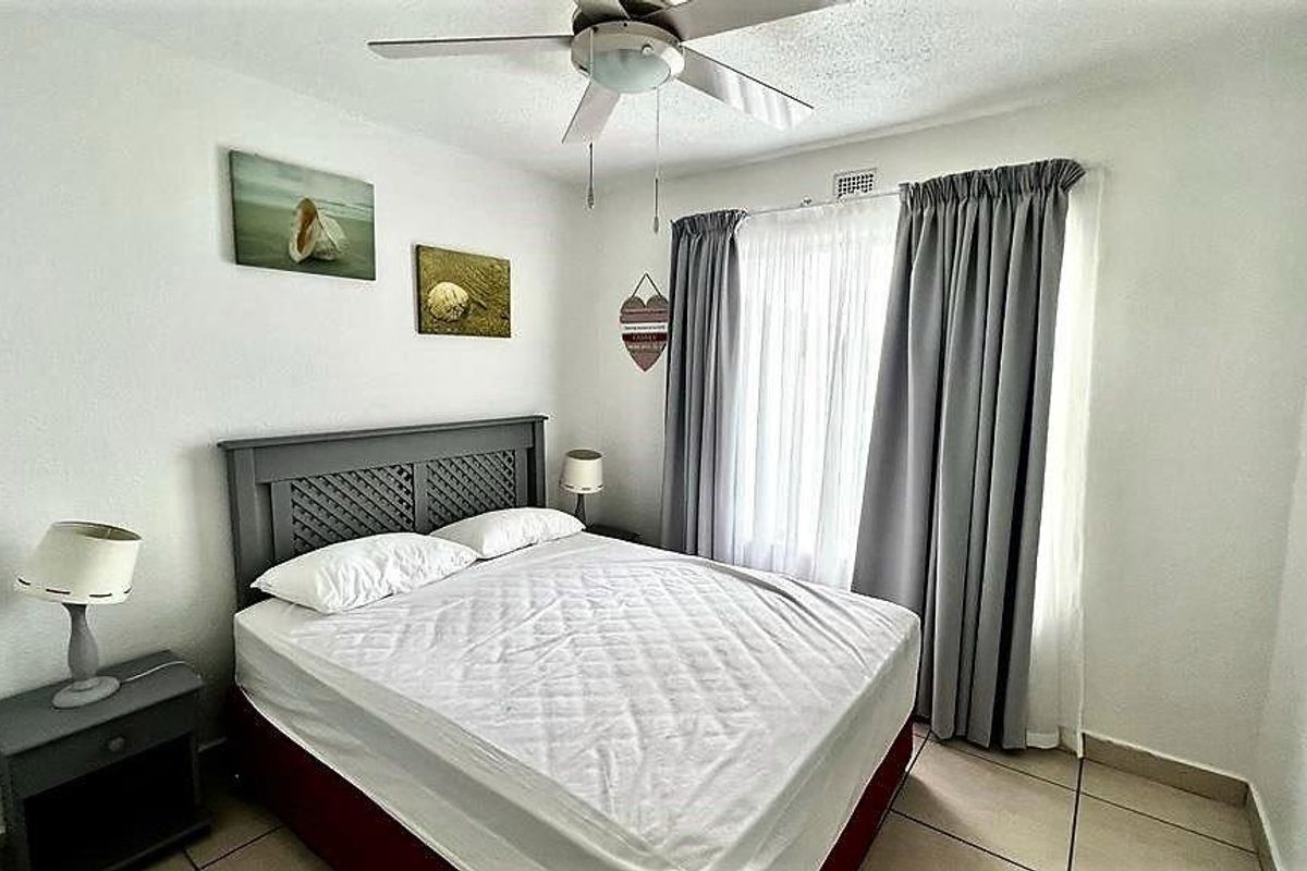 A functional bedroom featuring tiled flooring, a ceiling fan, and large windows with curtain tracks, providing a neutral space for rest.