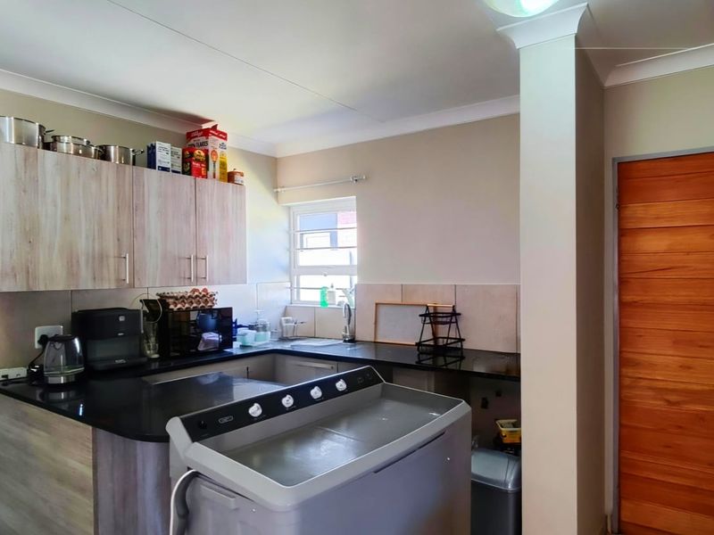 A functional scullery area featuring laminate cabinetry, granite countertops, a stainless steel sink, and a tiled splashback.