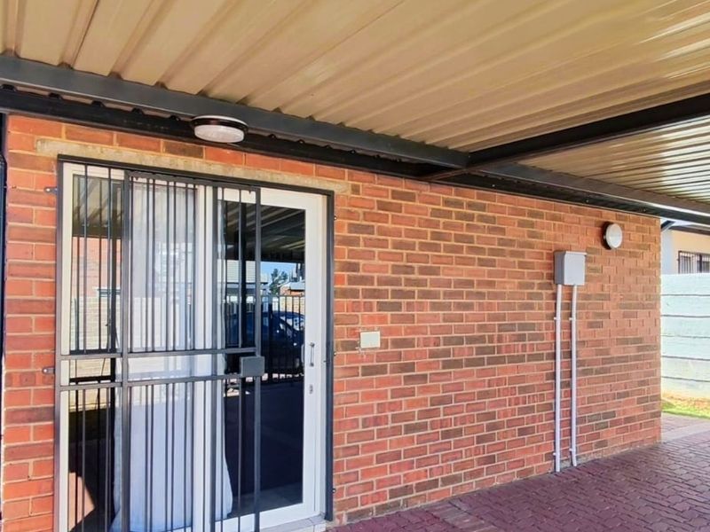 A covered carport area featuring a brick facade, paved flooring, and a secure sliding door entrance.