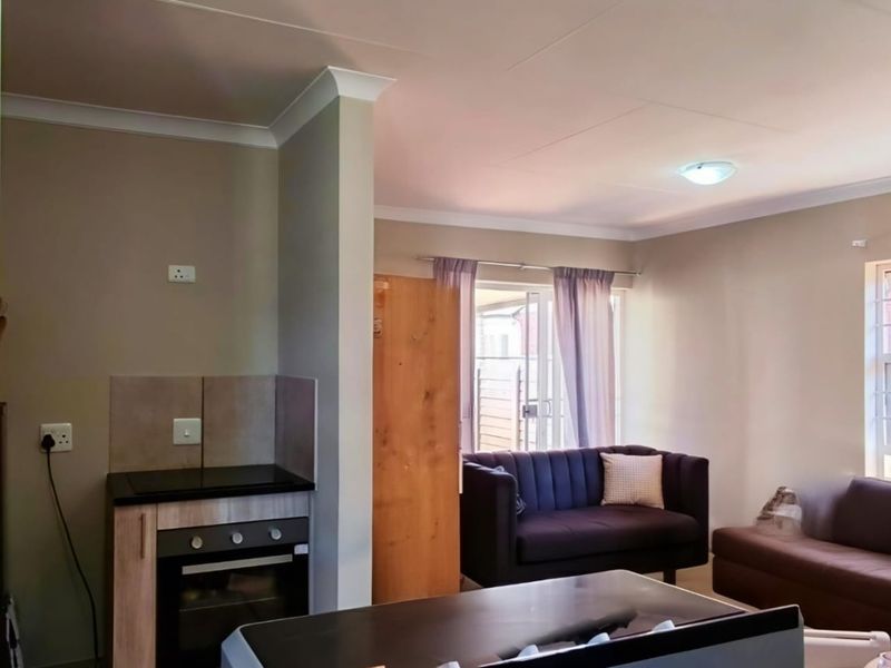 Open-plan living area featuring a compact kitchen with built-in oven and hob, tiled flooring, and direct access to the exterior via a sliding door.
