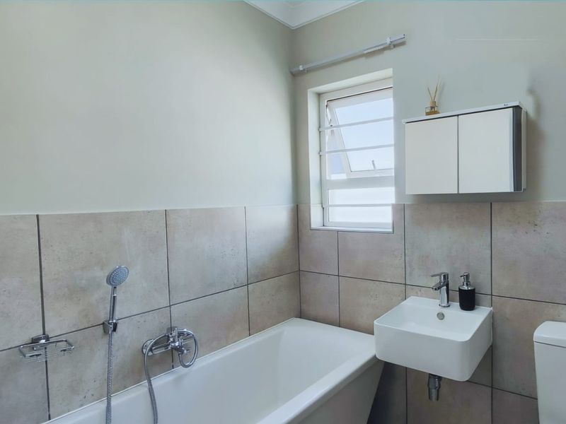 A clean and functional bathroom featuring a bathtub with shower mixer, wall-mounted basin, toilet, and a convenient medicine cabinet.