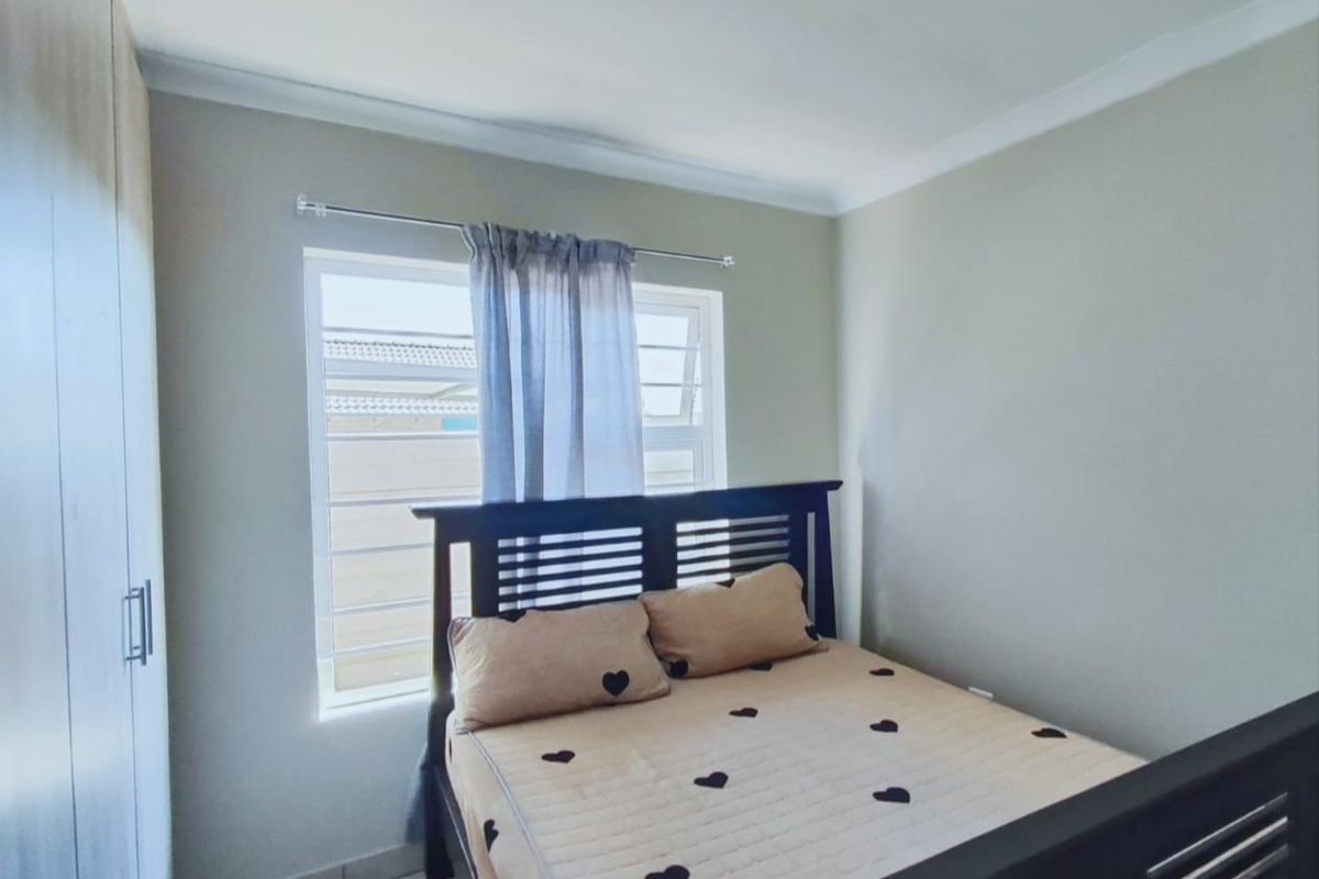 A well-maintained bedroom featuring a built-in wardrobe, neutral wall finishes, and a window fitted with security bars.