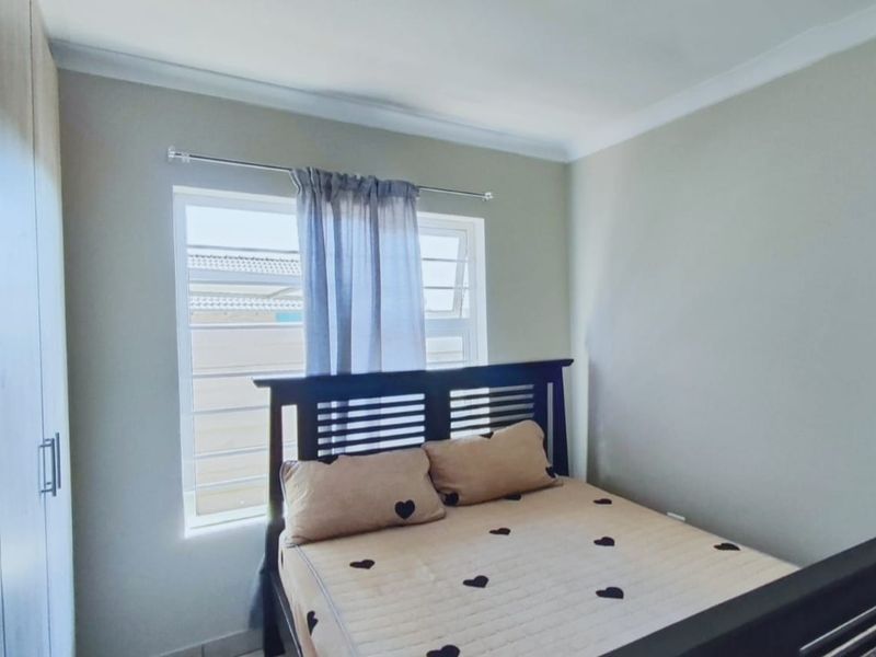 A well-maintained bedroom featuring a built-in wardrobe, neutral wall finishes, and a window fitted with security bars.